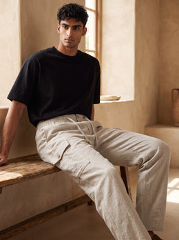 Seated lifestyle view of men’s cream cotton cargo pants showing the thigh cargo pocket