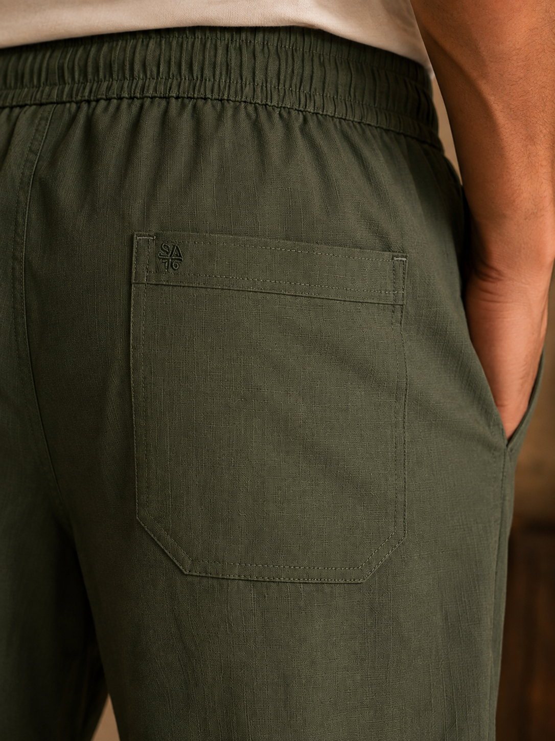 Close view of dark green pants elastic waistband, button and drawcord